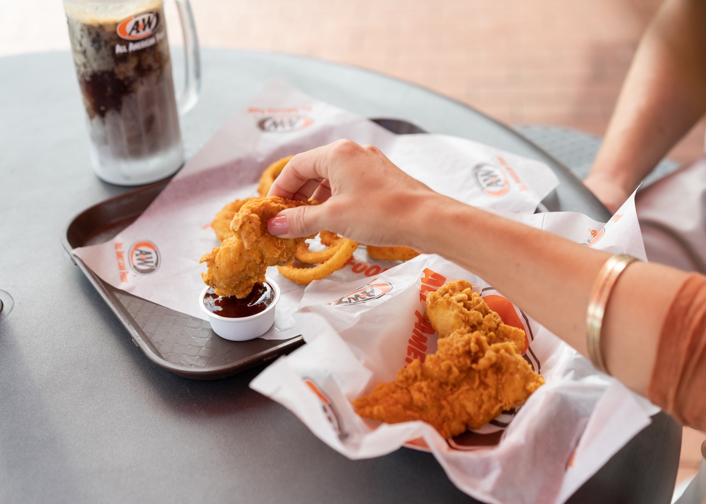 Person dipping Hand-Breaded Chicken Tender into BBQ Sauce